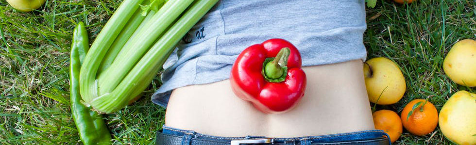 Frukt og grønnsaker strødd rundt magen til en liggende person. Foto.